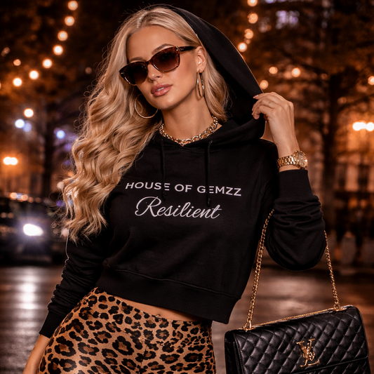 Woman wearing a black hoodie with text and leopard print pants, holding a black handbag on a street at night.