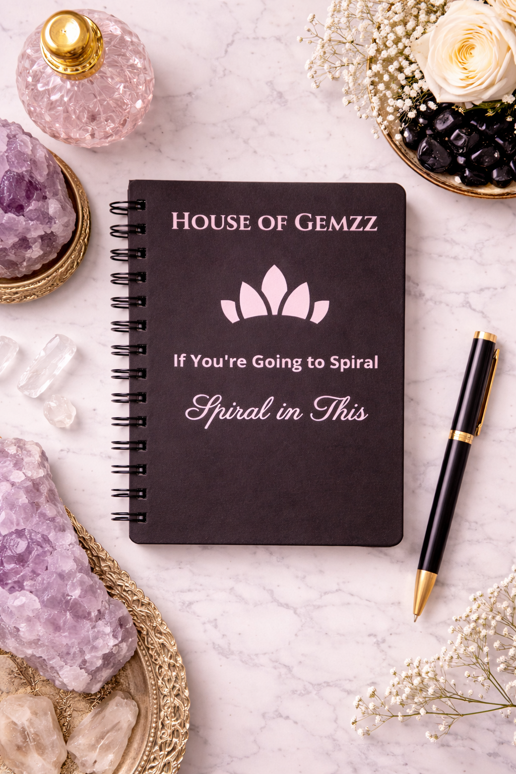 Black notebook with 'House of Gemzz' branding on a marble surface with crystals and flowers.